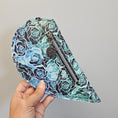Load image into Gallery viewer, Hand holding a floral-patterned fanny pack against a gray background