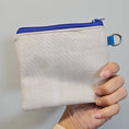 Load image into Gallery viewer, Beige pouch with blue zipper held by a hand against a light gray background