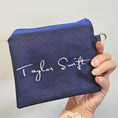 Load image into Gallery viewer, Hand holding a navy blue pouch with 'Taylor Swift' branding on a light gray background