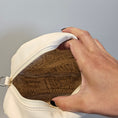 Load image into Gallery viewer, Hand holding a beige pouch with textured interior against a gray background