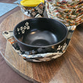 Load image into Gallery viewer, Black bowl with floral-patterned bowl cozy on a wooden surface.