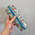 Load image into Gallery viewer, Hand holding a cylindrical pouch with a colorful pattern against a gray background