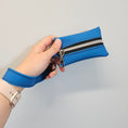 Load image into Gallery viewer, Hand holding a blue wallet with a zipper against a light gray background