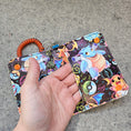 Load image into Gallery viewer, Colorful keychain with cartoon character held by a hand on a concrete surface