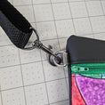 Load image into Gallery viewer, Close-up of a colorful pouch with a black strap and metal clasp on a grid background