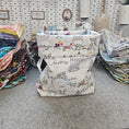 Load image into Gallery viewer, Stack of patterned fabric swatches on a gray surface with a pegboard in the background.