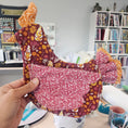Load image into Gallery viewer, Hand holding fabric samples with floral patterns in a craft store setting