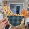 Load image into Gallery viewer, Handmade hot pad with floral and checkered patterns held in front of a television.