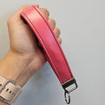 Load image into Gallery viewer, Pink leather strap with a metal buckle held in a hand against a neutral background