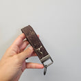 Load image into Gallery viewer, Gold and brown cork key fob against a light gray wall.