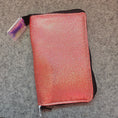 Load image into Gallery viewer, A rectangular zippered pouch with a textured, iridescent metallic finish that shifts from pink to orange, featuring a black fabric lining and a small holographic tag attached near the top left corner.