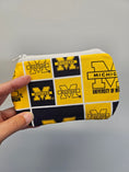 Load image into Gallery viewer, Hand holding a university of michigan mini zipper pouch against a light blue wall.