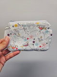 Load image into Gallery viewer, A hand holding a zippered pouch with a white background and a colorful cartoon bird and flower pattern, set against a plain gray wall.