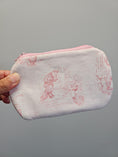 Load image into Gallery viewer, A hand holding a small zippered pouch made of white fabric with a pink sketch print and a pink zipper, shown against a plain gray background.