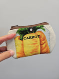 Load image into Gallery viewer, A hand holding a small zippered pouch with a printed illustration of a carrot on a light gray background.