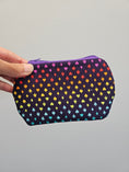 Load image into Gallery viewer, A hand holding a small zippered pouch with a dark purple background and a repeating pattern of small hearts in rainbow colors, against a plain light gray background.