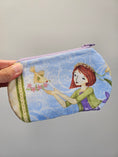 Load image into Gallery viewer, A fabric zippered pouch held by a hand, featuring a whimsical illustration of a girl with red hair, a bird, and flowers on a light blue background.