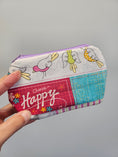 Load image into Gallery viewer, A hand holding a small zippered fabric pouch with a patchwork design featuring cartoon birds, a pink panel with the words 'Choose Happy,' and a turquoise textured section, against a plain light gray background.