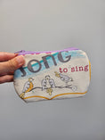 Load image into Gallery viewer, A hand holding a small fabric zip pouch with a whimsical bird illustration and the words 'song to sing' on a plain gray background.
