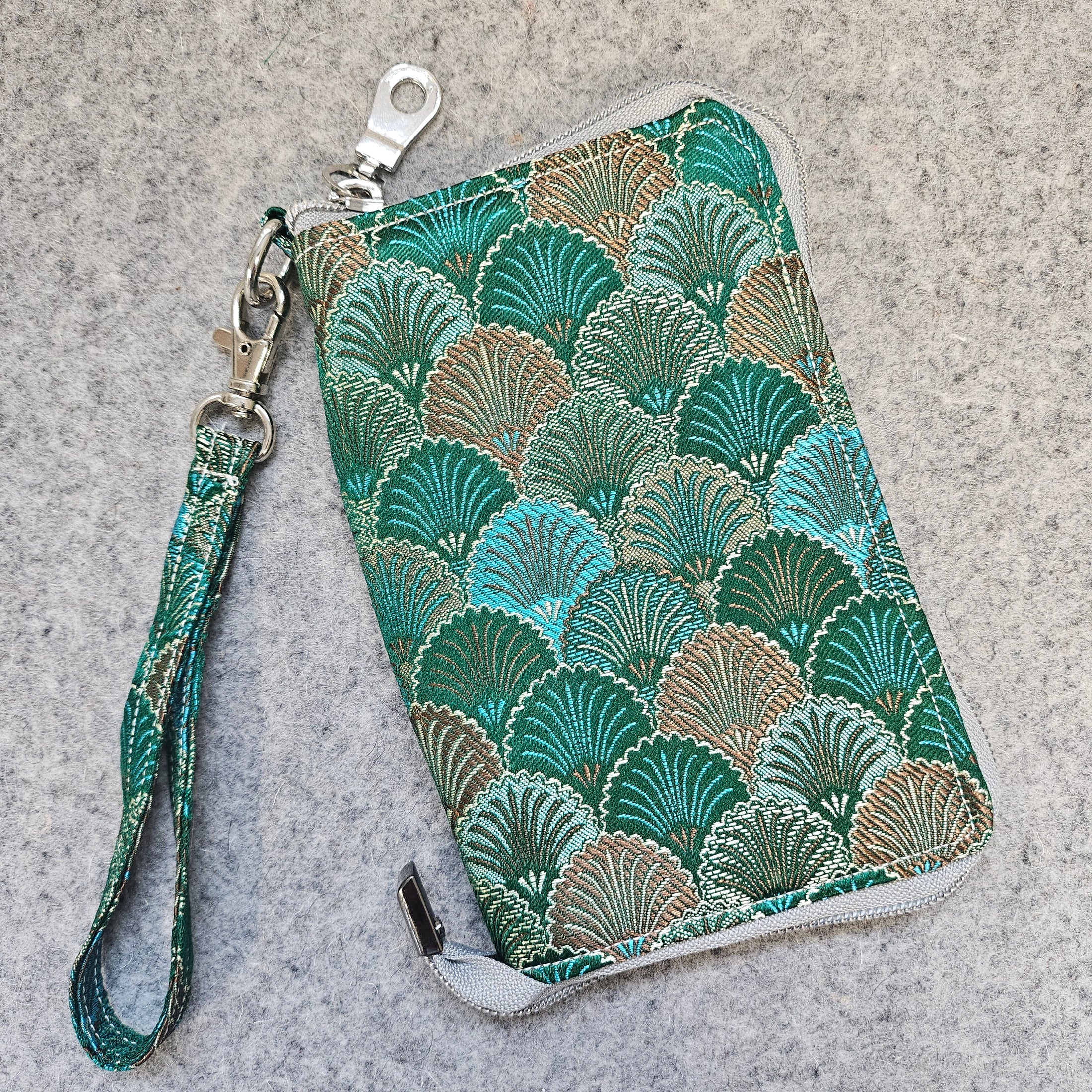 Green patterned clutch with a wrist strap on a gray surface
