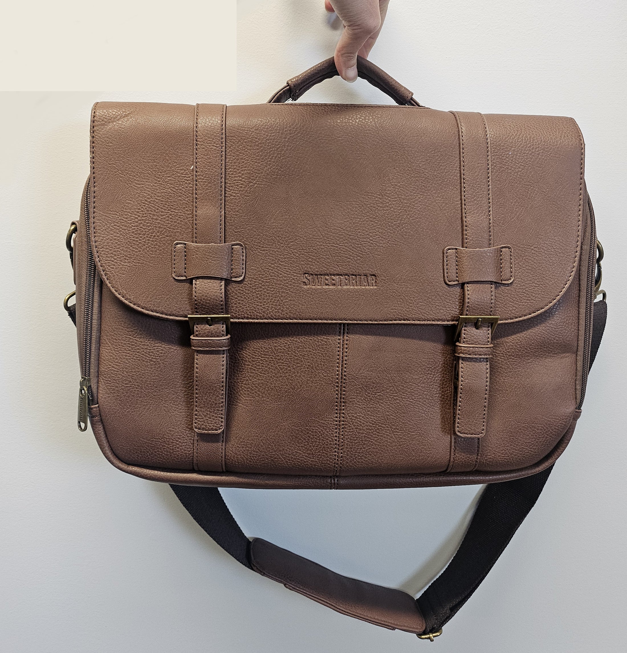 Brown leather satchel bag held by a hand on a light gray background