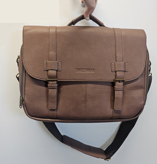 Brown leather satchel bag held by a hand on a light gray background