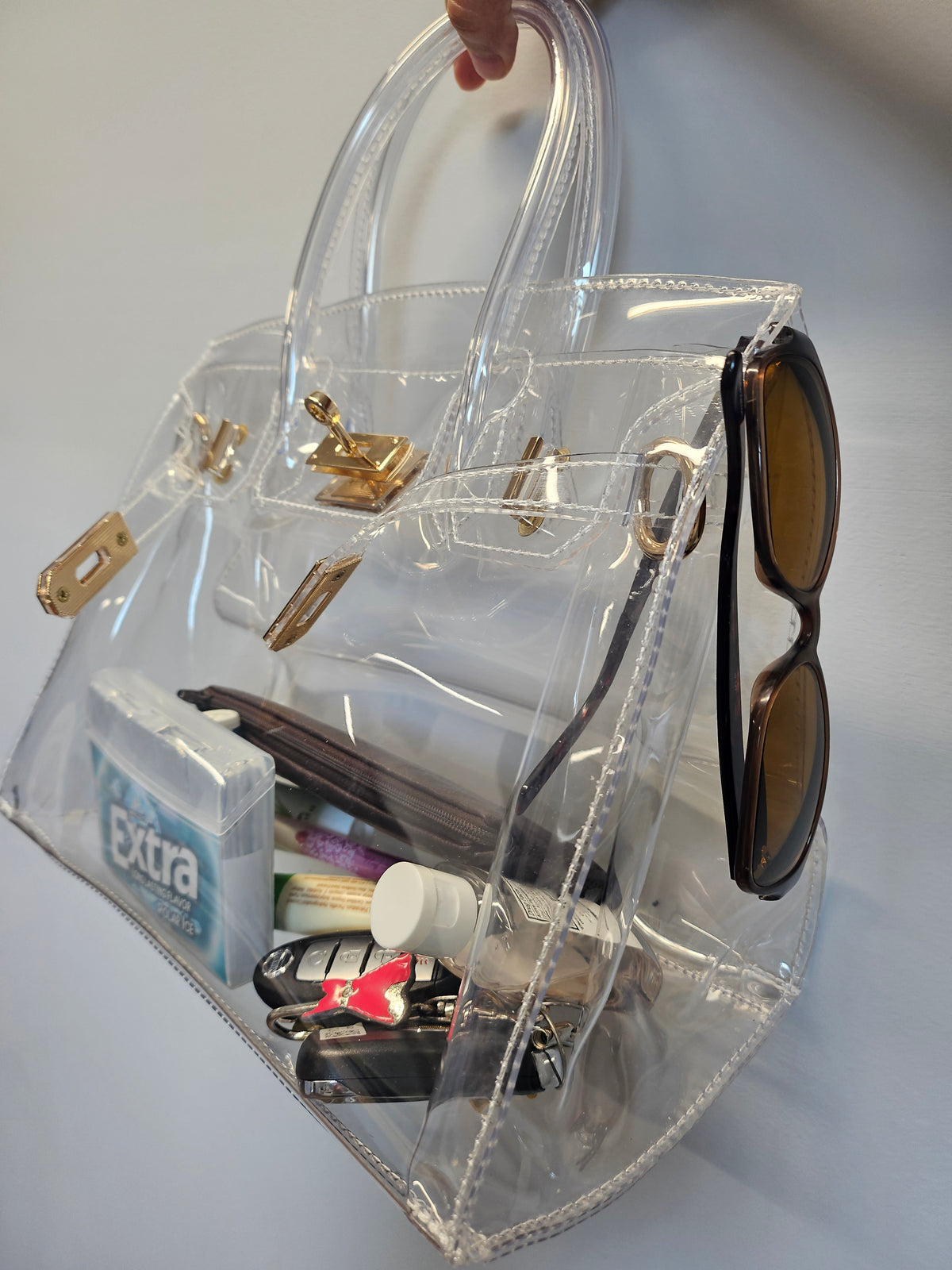 Clear stadium bag filled with personal items against a light gray wall.