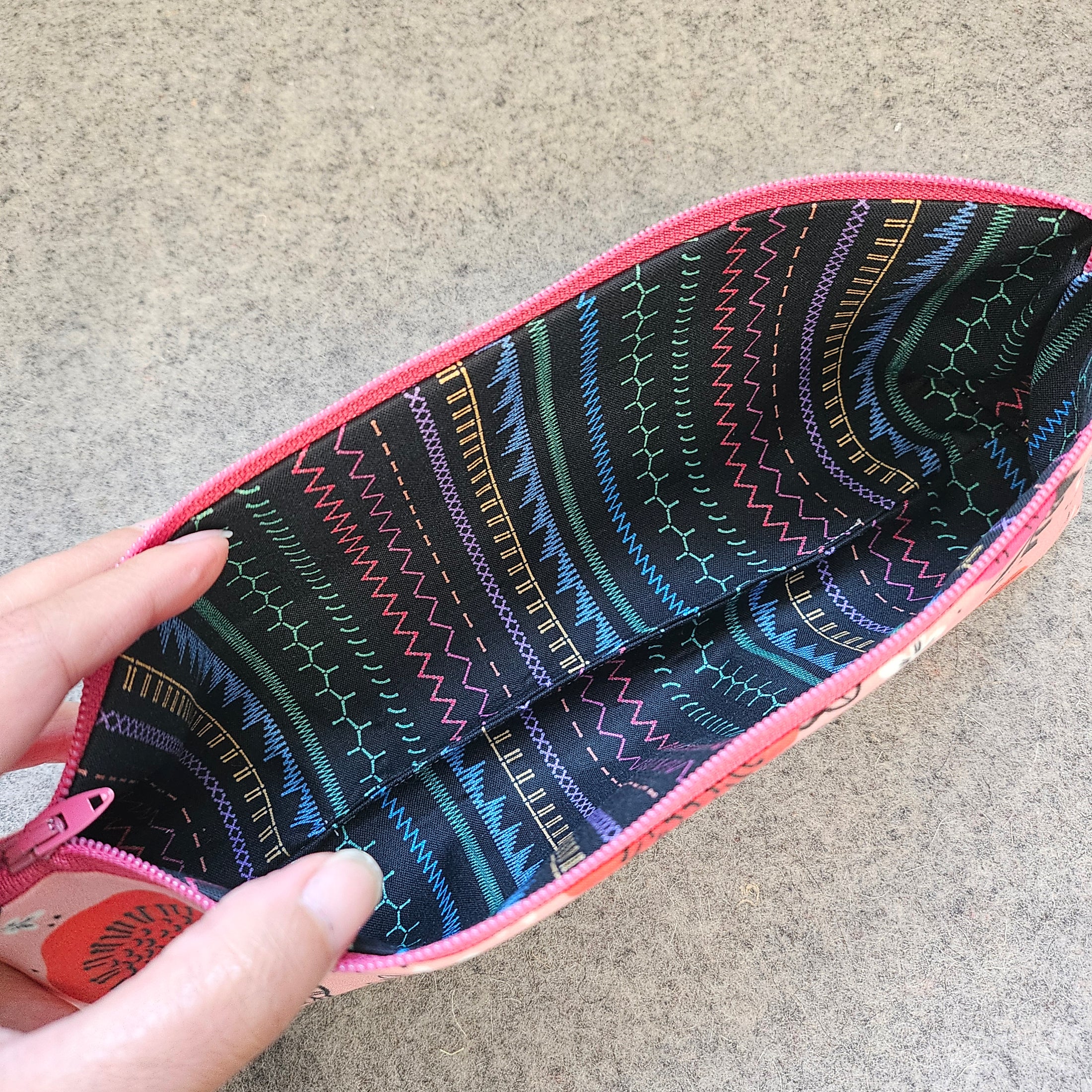 Lining fabric of the praise be bitches zipper pouch is black with multicolored stitch designs.