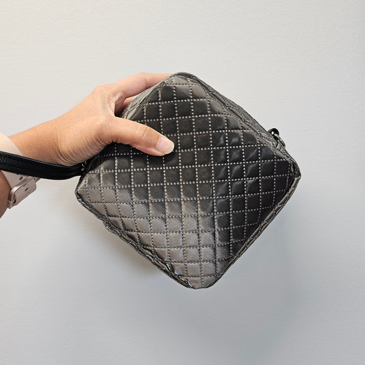Hand holding a quilted gray pouch against a light gray background