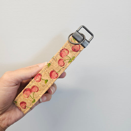 Cork keychain with cherry pattern held by a hand against a light gray background