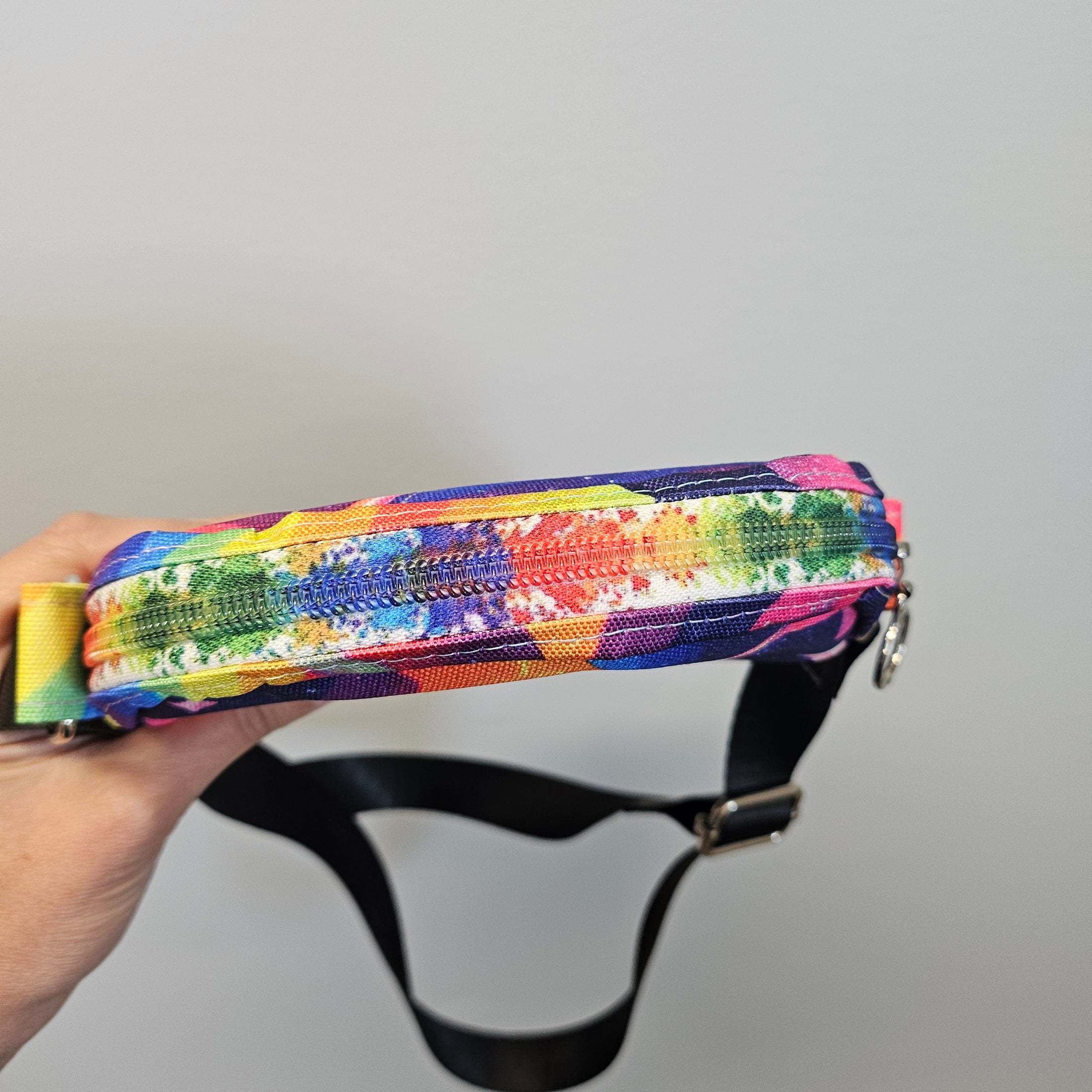 Colorful patterned strap with a black buckle held by a hand against a gray background