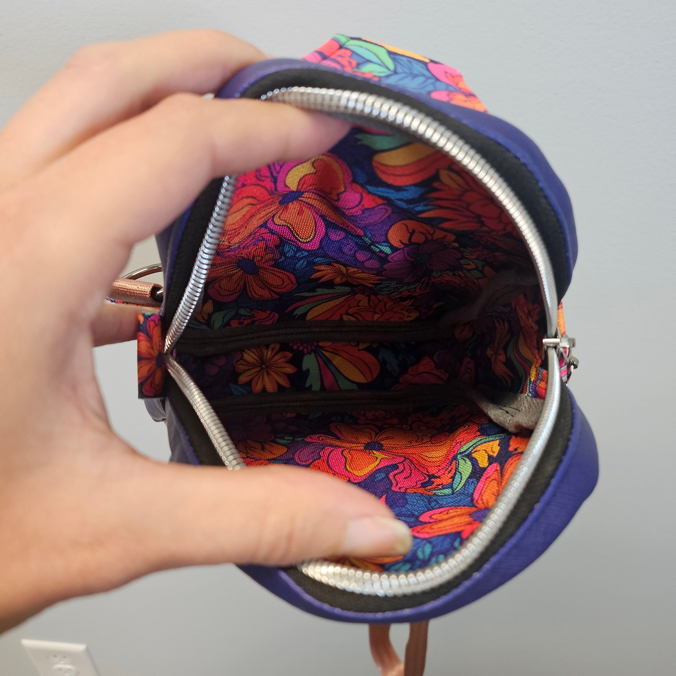 Colorful floral-patterned purse held by a hand against a neutral background