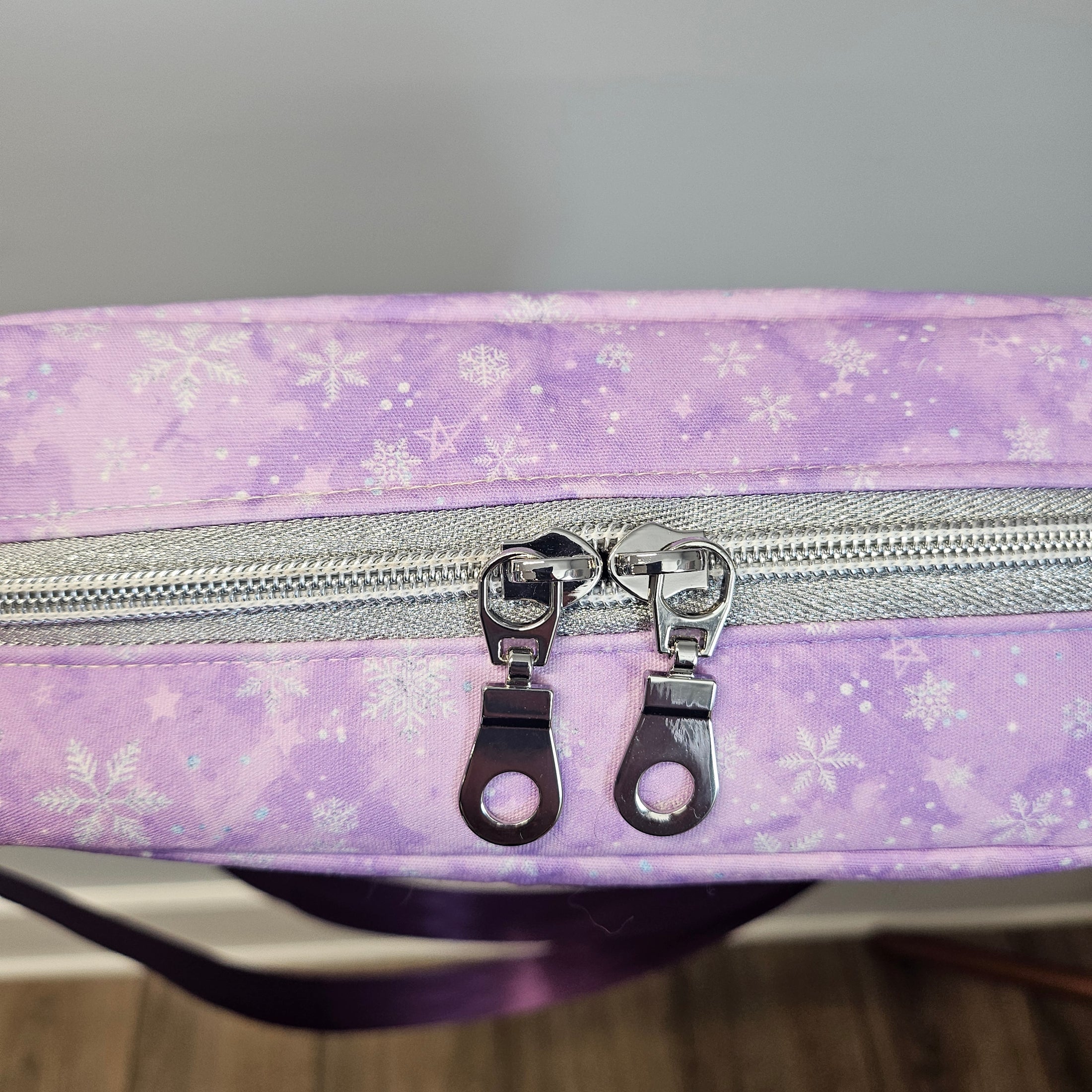 Purple bag with snowflake pattern and silver zipper on a neutral background