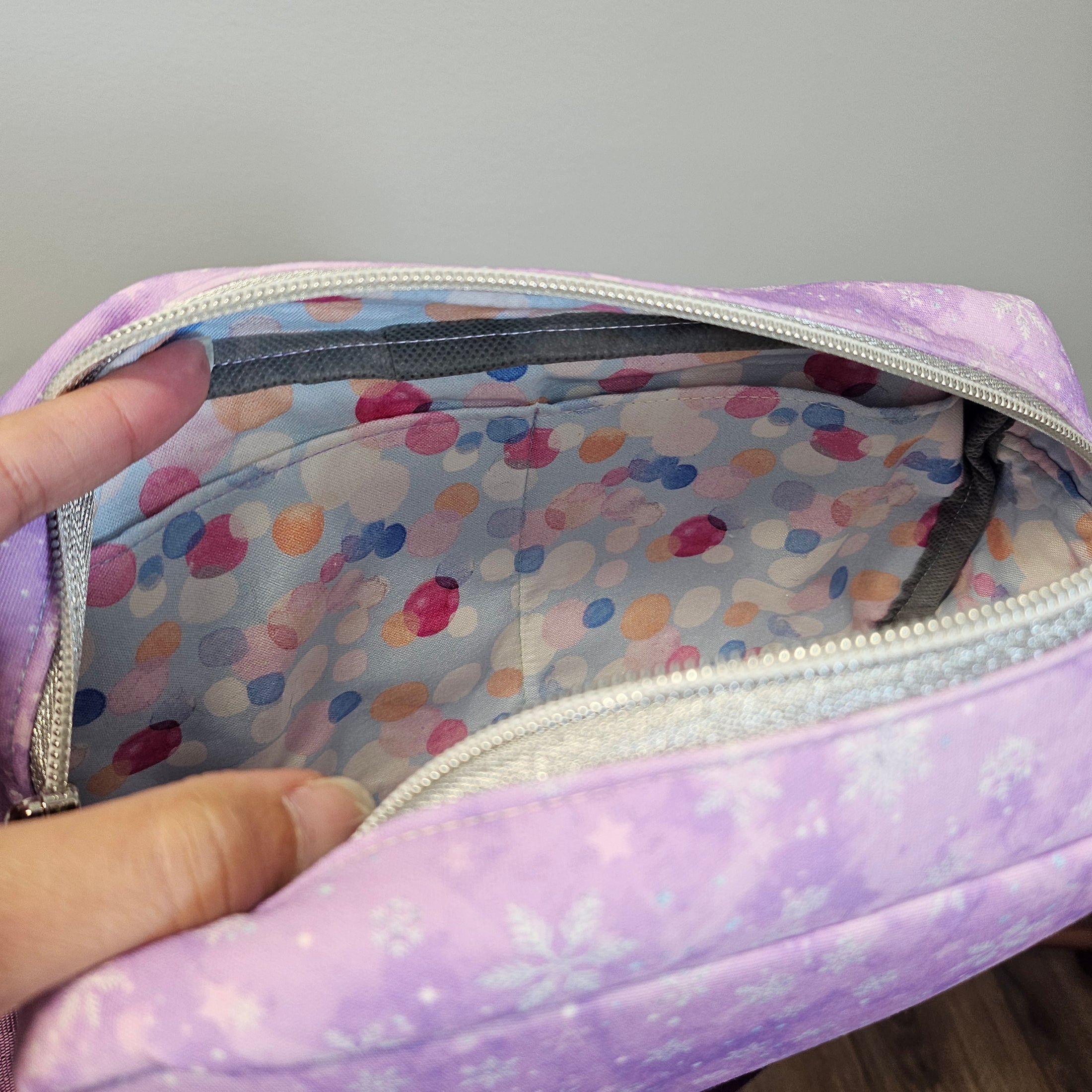 Purple pouch with colorful polka dot interior held by a hand against a neutral background
