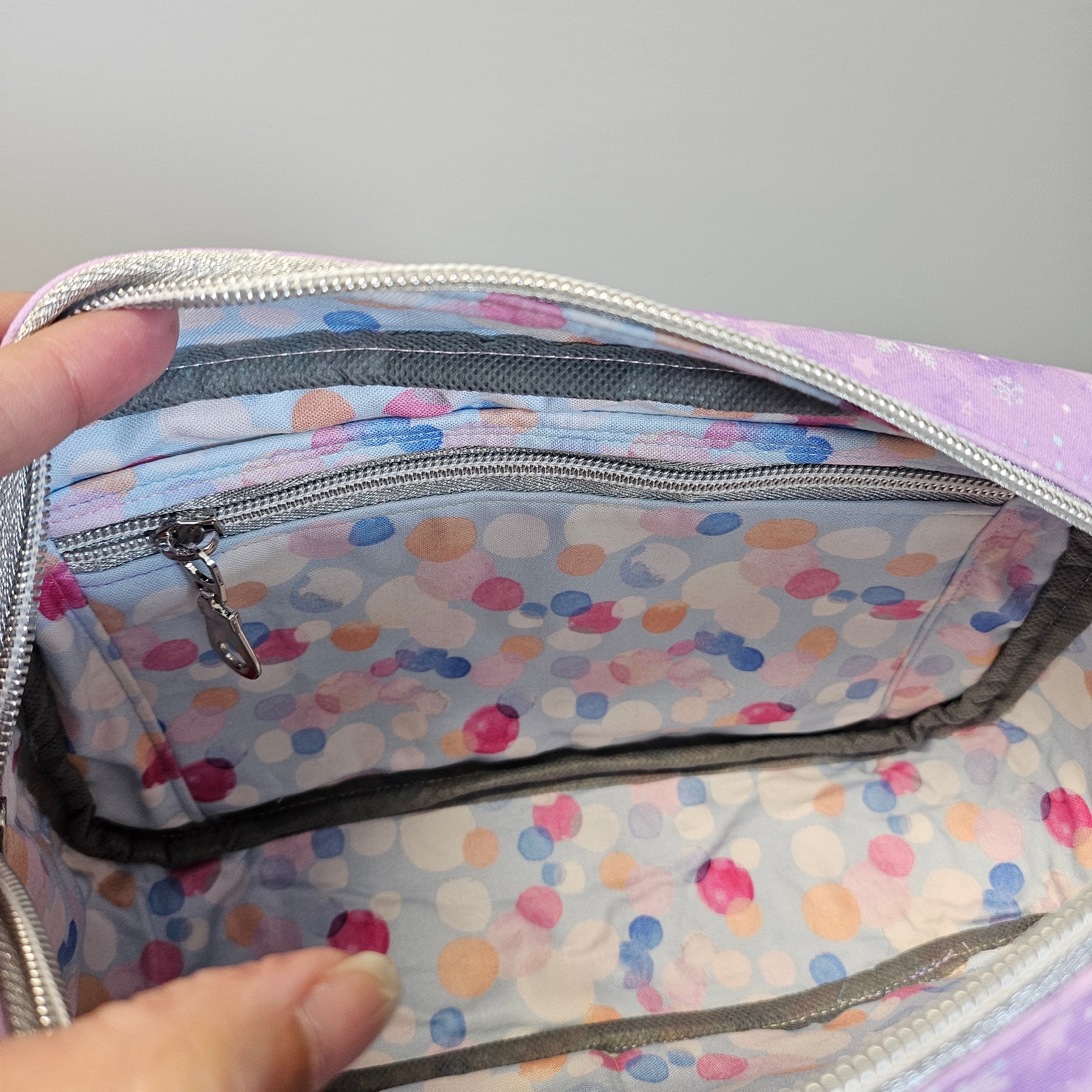 Colorful polka dot bag with a hand opening it on a gray background