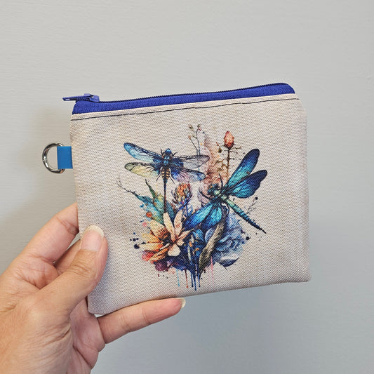 Hand holding a small pouch with dragonfly design against a gray background