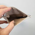 Load image into Gallery viewer, Hand holding an empty beige wallet against a light gray background
