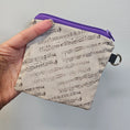 Load image into Gallery viewer, Hand holding a small pouch with music sheet design and purple zipper against a gray background
