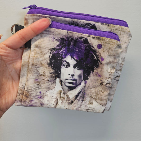 Hand holding a wallet with a purple zipper and artistic design on the cover.