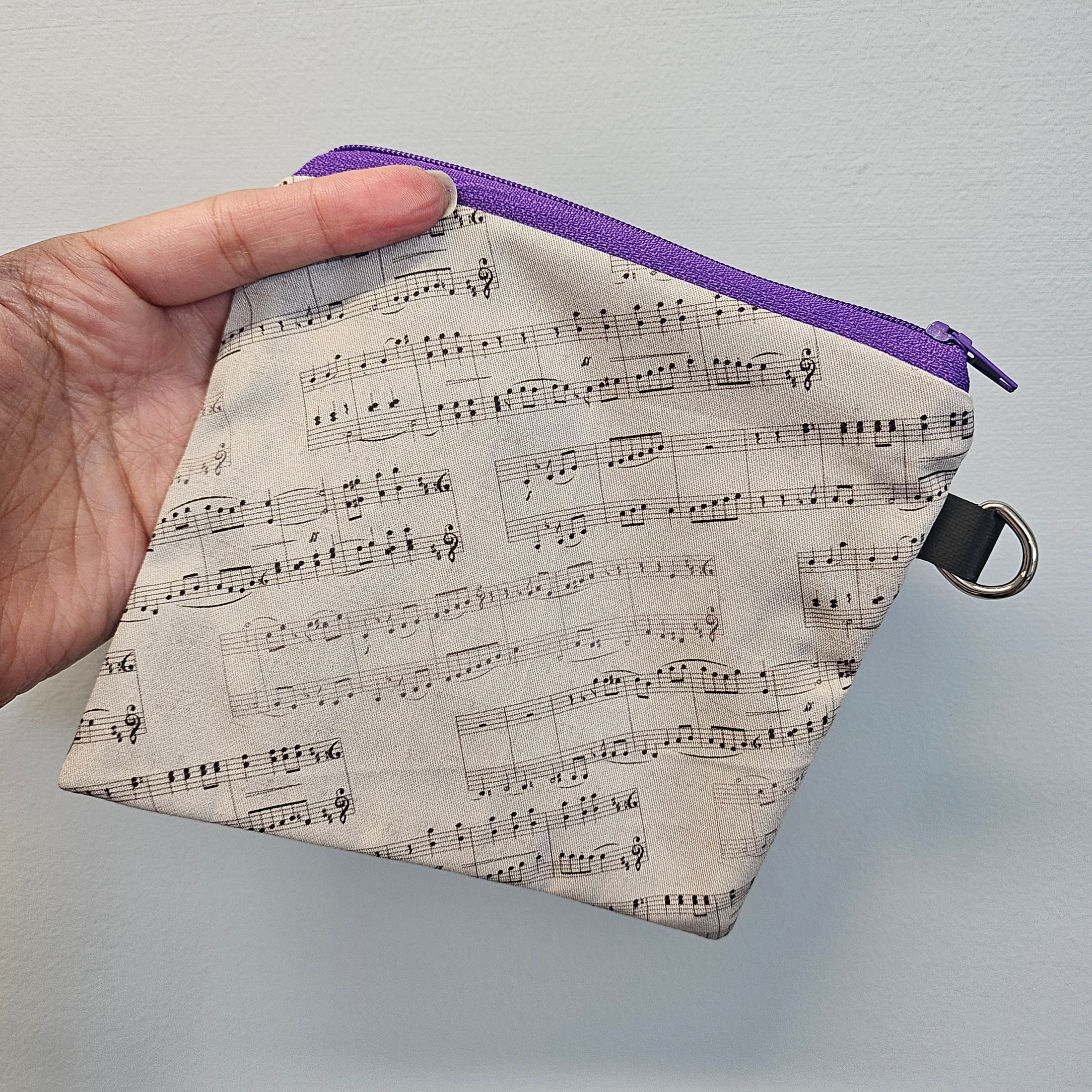 Small pouch with music note pattern held by a hand against a gray background