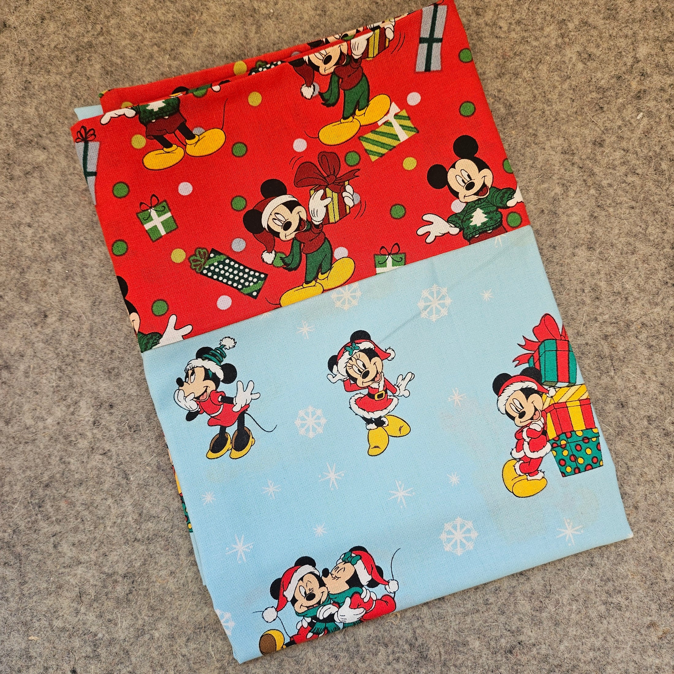 Two sheets of Christmas-themed wrapping paper with cartoon characters on a textured surface.