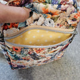 Load image into Gallery viewer, Floral-patterned cosmetic bag with a yellow interior on a gray background
