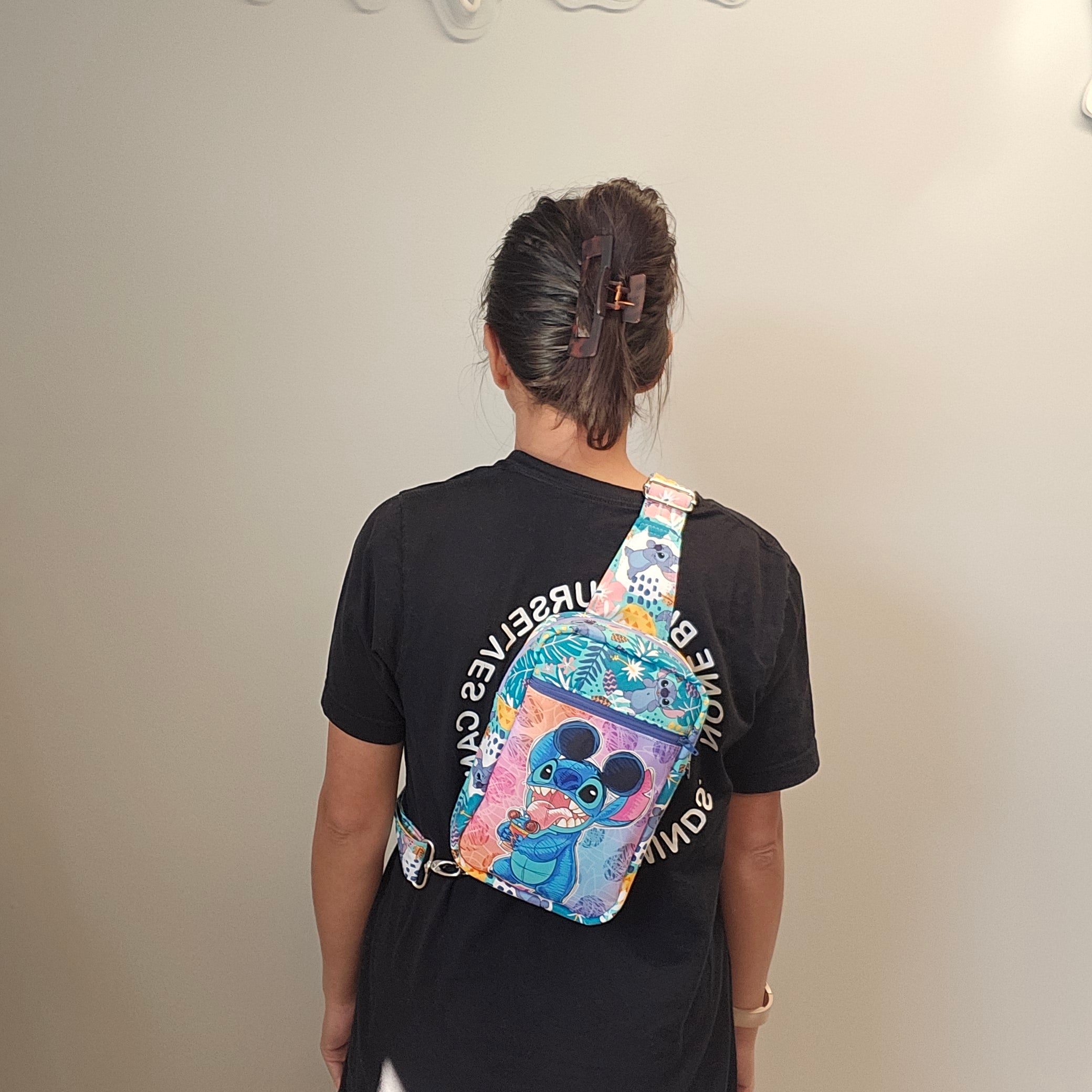 Person wearing a black shirt with a colorful patterned bag over their shoulder against a plain background