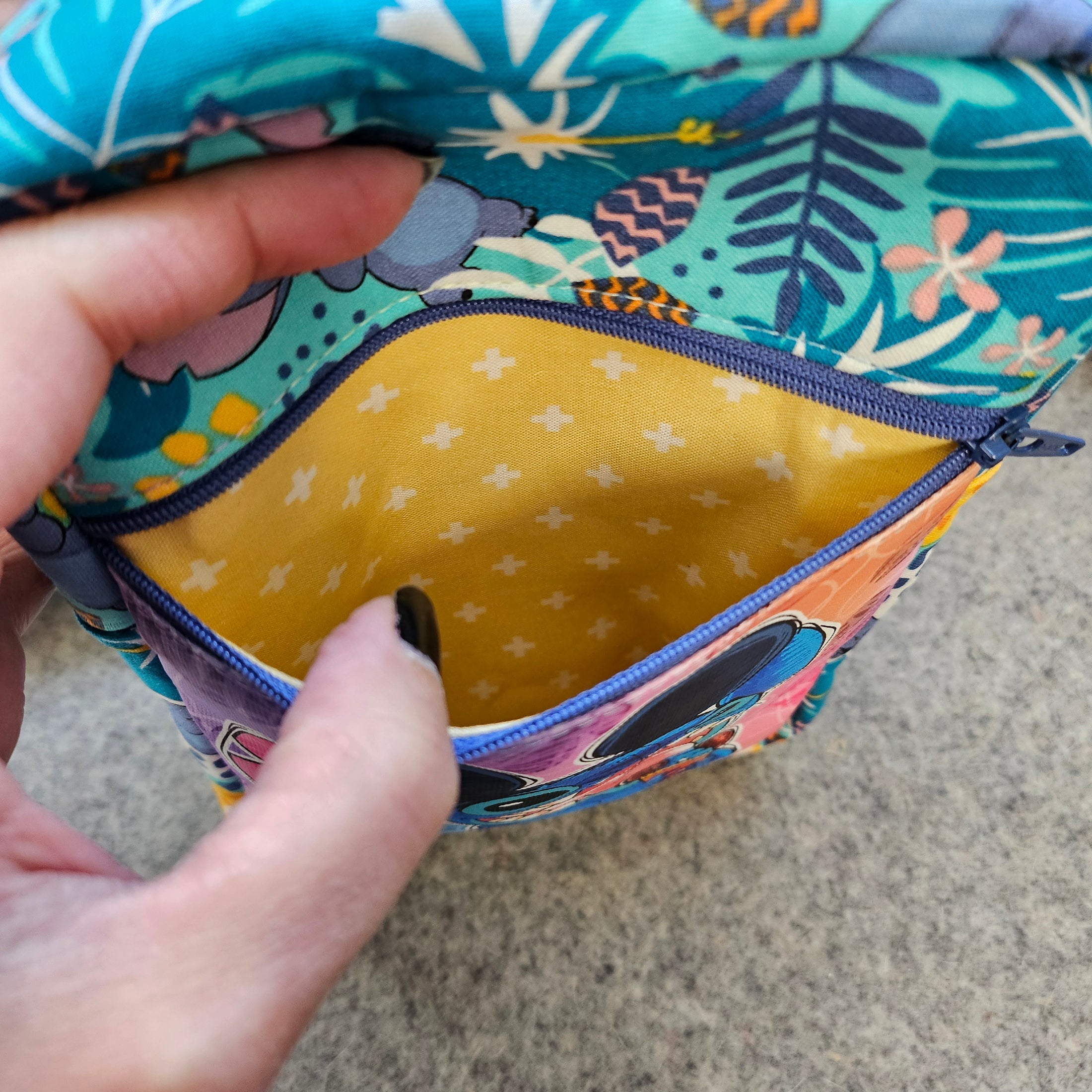 Colorful fabric pouch with floral and animal patterns, held by a hand.