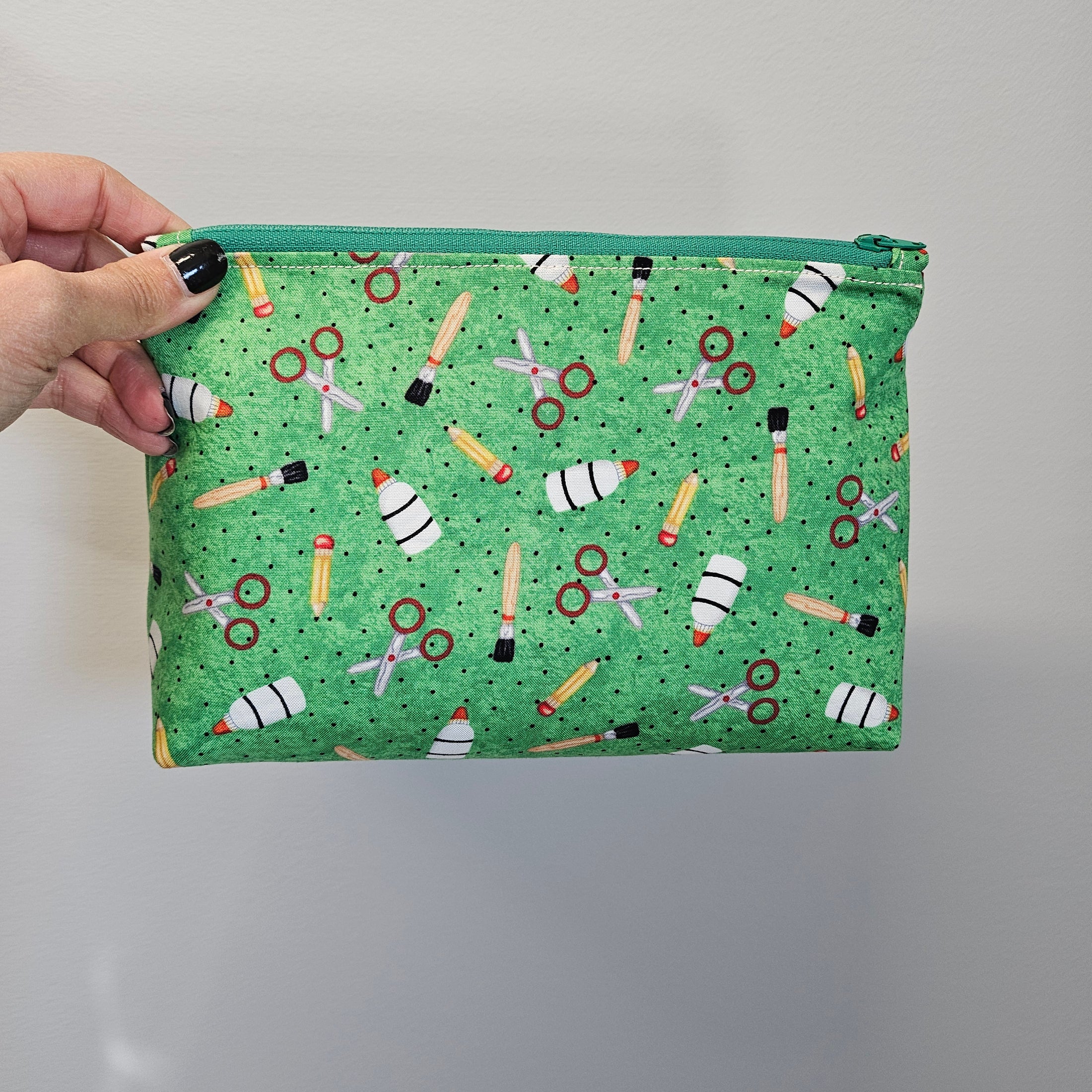 Green zipper pouch with school supplies shown on the outside.