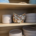 Load image into Gallery viewer, Stack of floral-patterned bowl cozies in a wooden drawer with other bowls.

