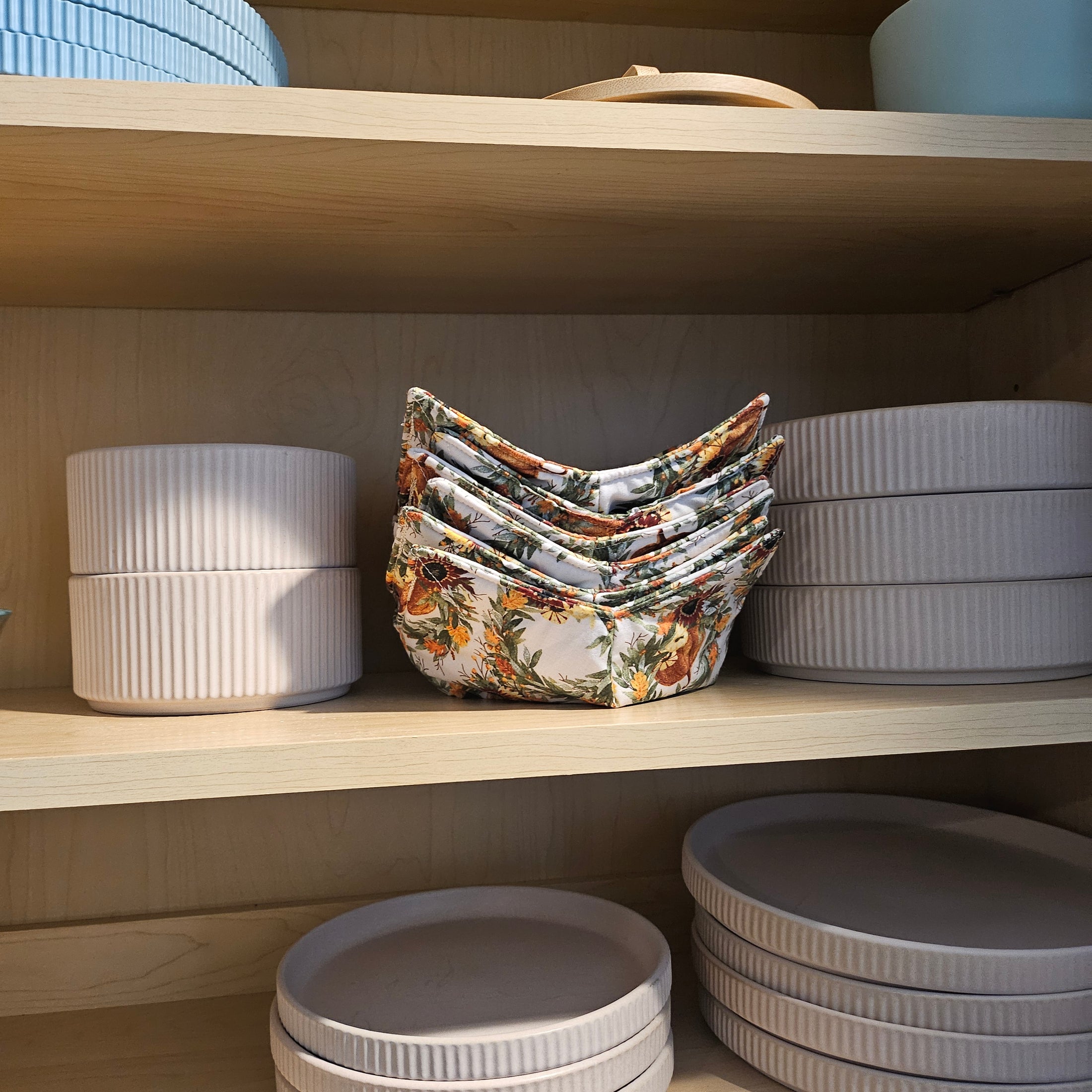 Stack of floral-patterned bowl cozies in a wooden drawer with other bowls.