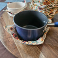 Load image into Gallery viewer, Black pot with floral pot holder on a wooden surface
