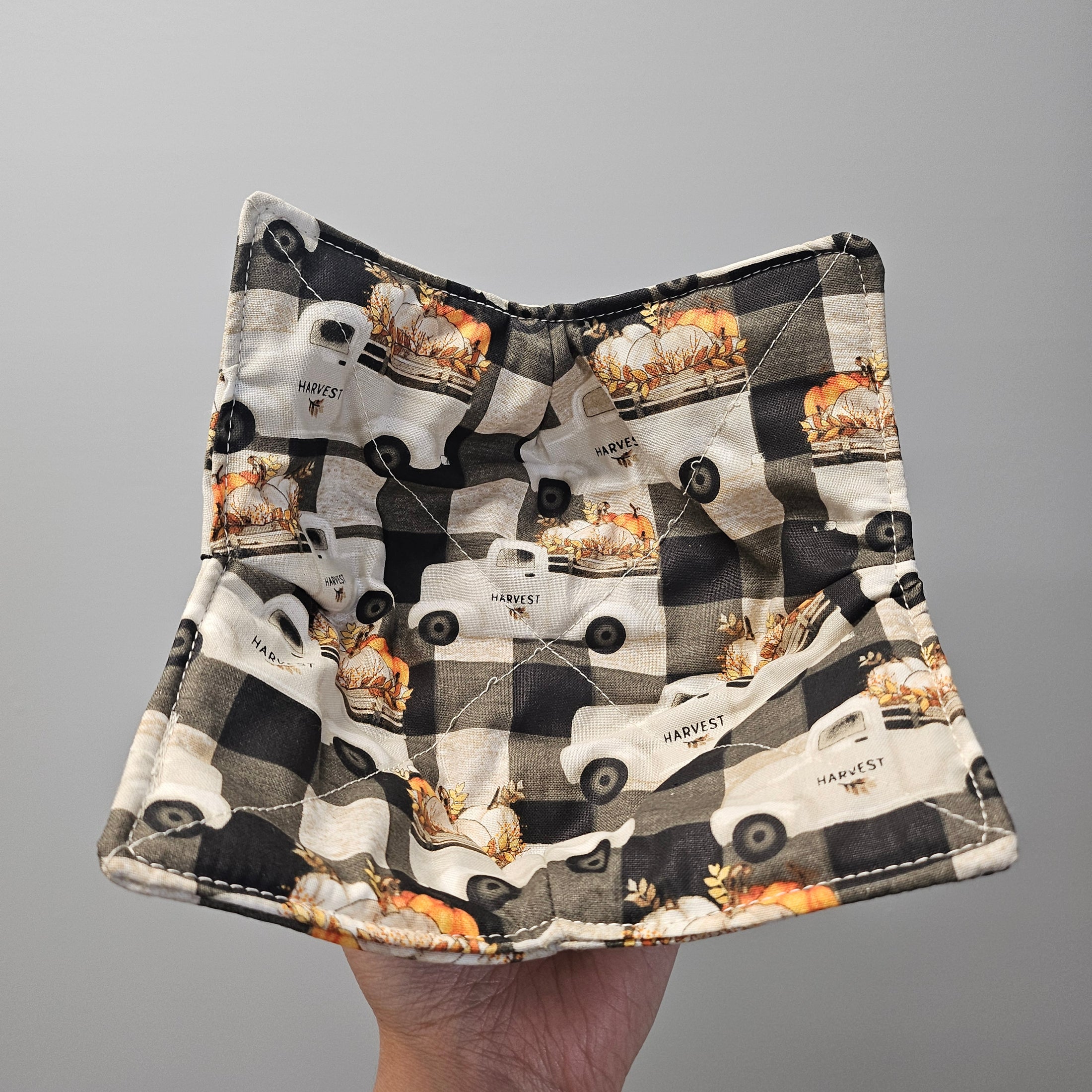 Fabric with black and white checkered pattern and truck illustrations held by a hand on a gray background