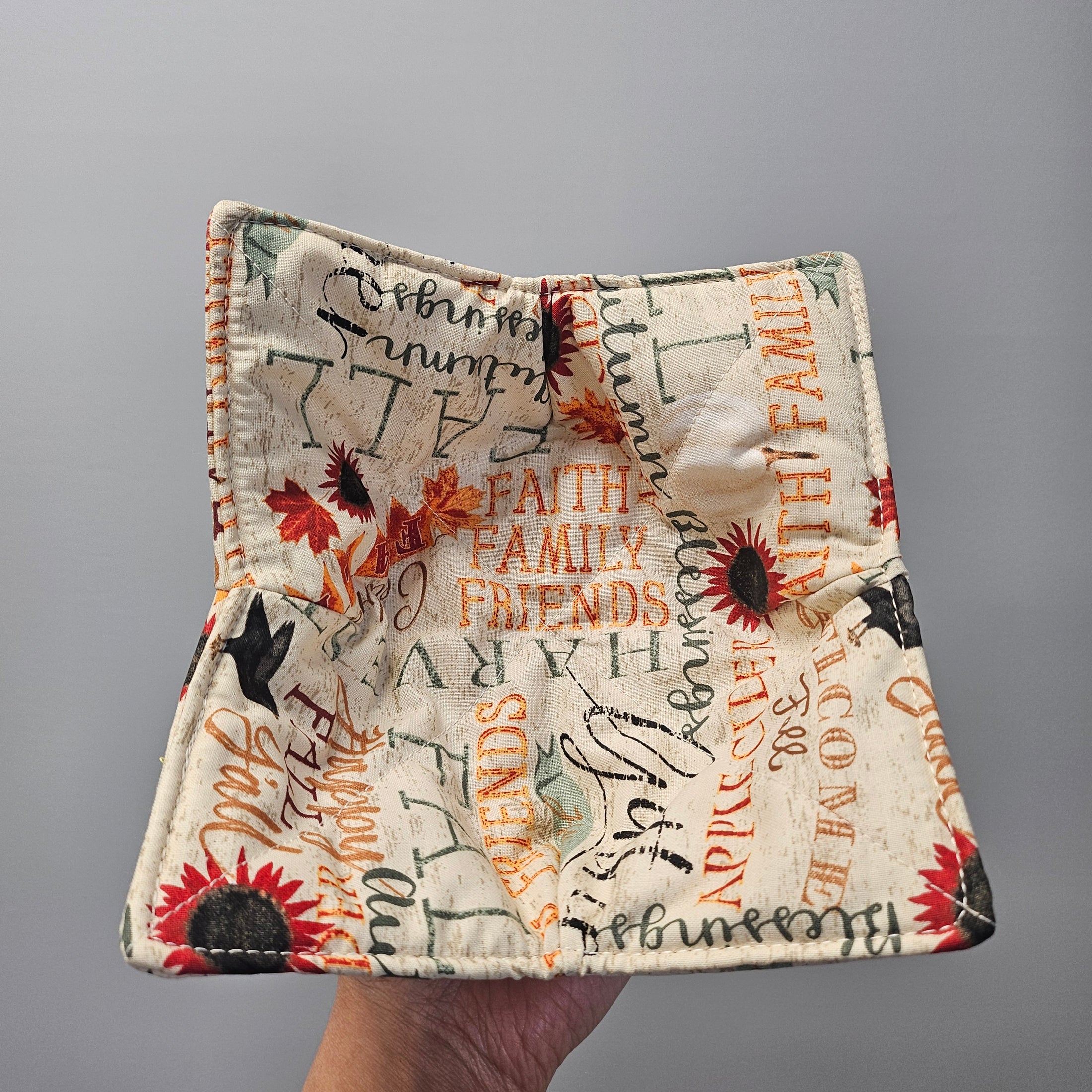 Fabric square with autumn-themed text and designs held against a gray background